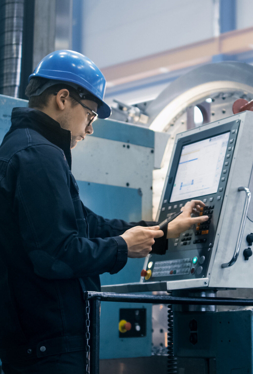 CNC-operatør med blå hjelm som justerer innstillinger på skjermen til en CNC-maskin.