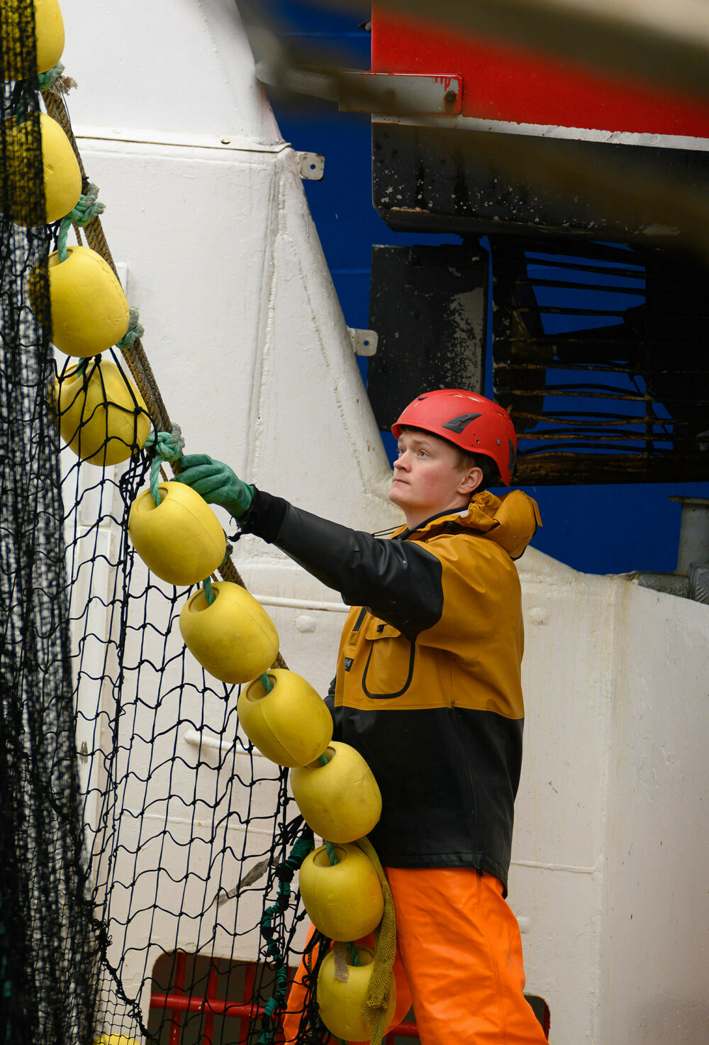 Fiskeredskapsarbeider tar imot not med gule korker fra en en fiskebåt.